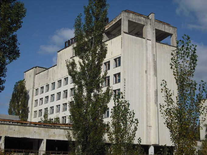 Vemos un edificio con muchas ventanas y algo alto, tiene vegetación por los lados de la construcción