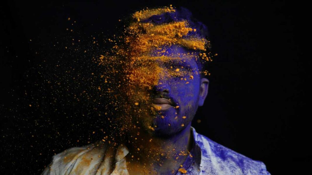 Retrato de persona cubierta de polvo azul y naranja en fondo negro