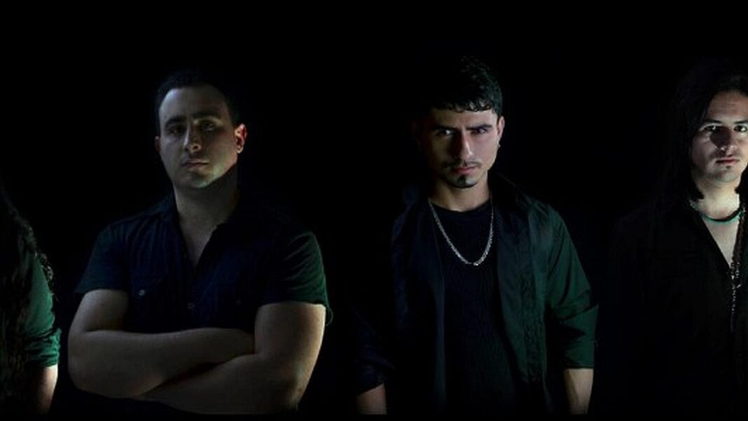 Tres hombres de pie sobre fondo negro con iluminación dramática; uno cruza los brazos y otro lleva cadena, con una persona parcialmente visible a la izquierda.