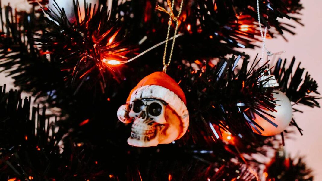 Árbol de Navidad negro con luces naranjas y un adorno con forma de calavera que lleva un gorro de Papá Noel, junto a una esfera blanca.