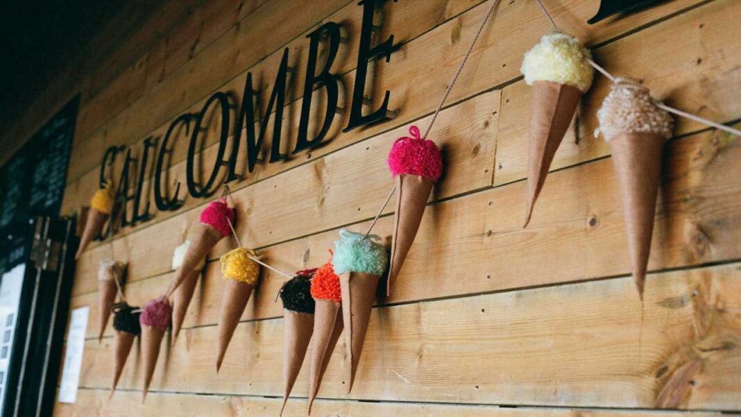 Pared de madera con letras grandes negras y una guirnalda de conos de cartón con bolas de lana de colores colgados con cuerdas.