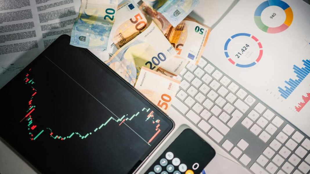 Tableta con gráfico de velas junto a billetes de euro, teclado blanco, calculadora y documentos con gráficos circulares y de barras.
