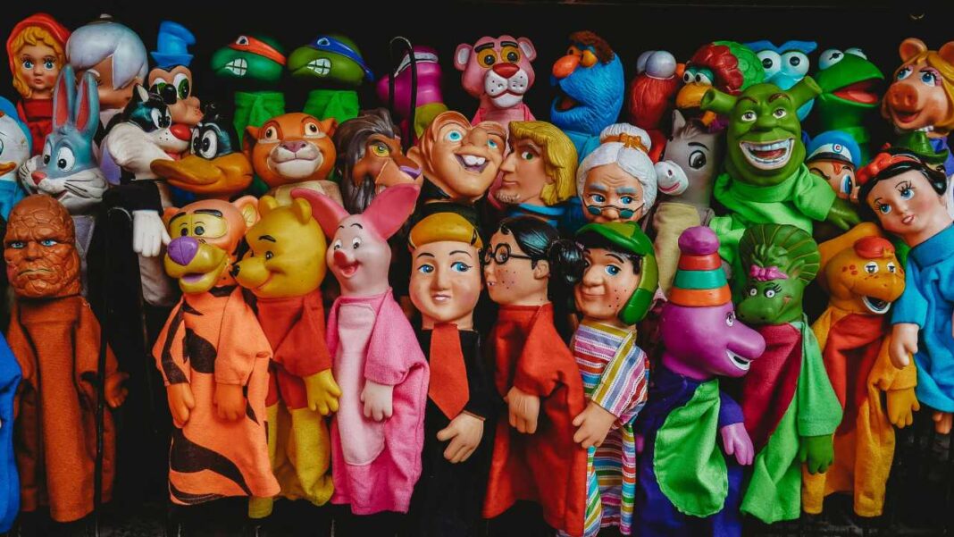 Gran grupo de marionetas de mano de colores alineadas sobre fondo oscuro, con personajes de rostros caricaturescos y trajes variados.