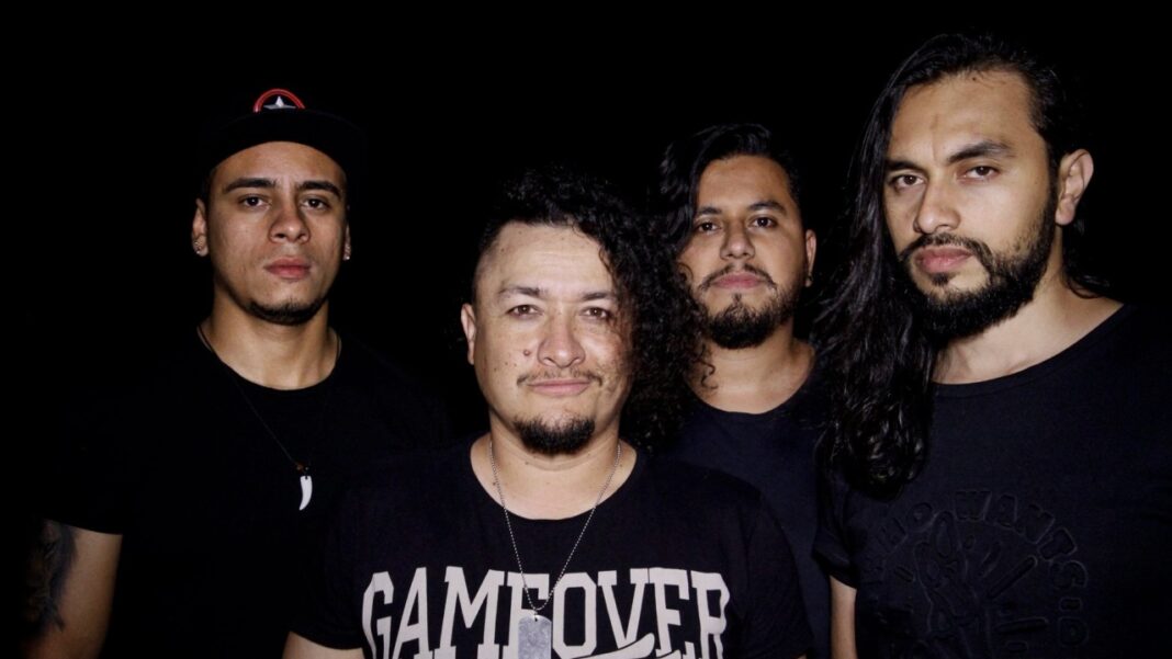 Cuatro hombres de pelo oscuro posan juntos ante un fondo negro; uno lleva camiseta negra con la frase GAME OVER y otro una gorra.