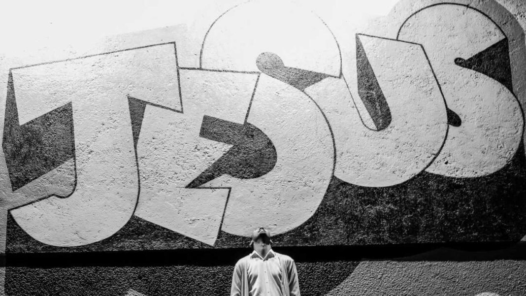 Mural en blanco y negro con letras enormes pintadas sobre una pared texturizada y una persona de pie debajo, en primer plano.