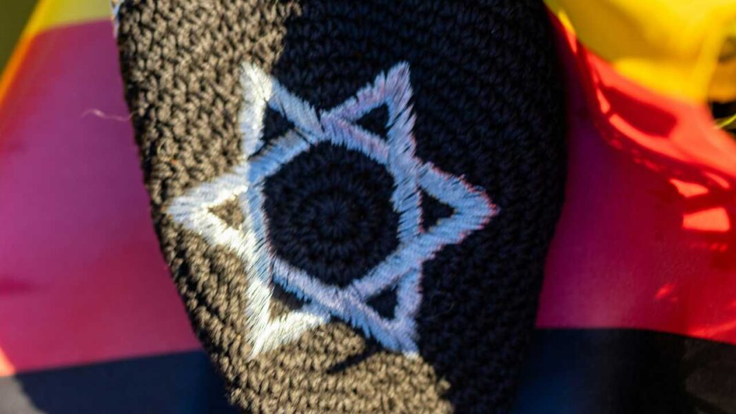 Parche bordado negro con una estrella de David en hilo claro, colocado sobre tela con franjas de colores vivos.