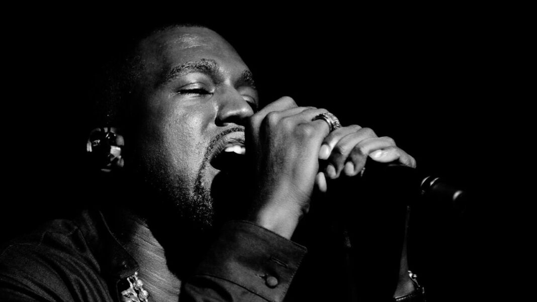 Primer plano en blanco y negro de un hombre con barba cantando con los ojos cerrados frente a un micrófono, sobre fondo oscuro.