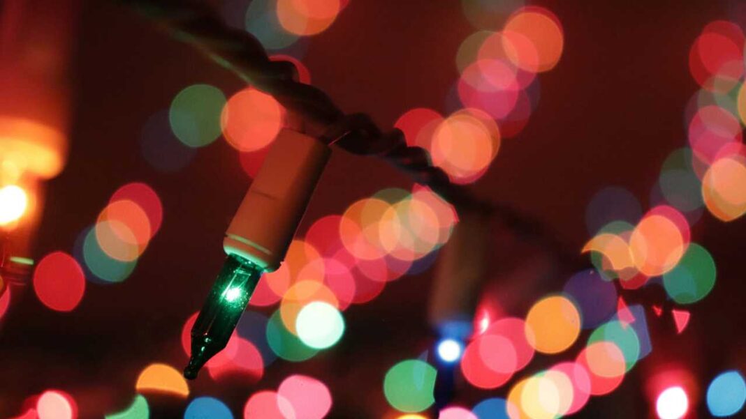 Primer plano de una guirnalda de luces navideñas con una bombilla verde enfocada y círculos desenfocados de colores sobre fondo oscuro.