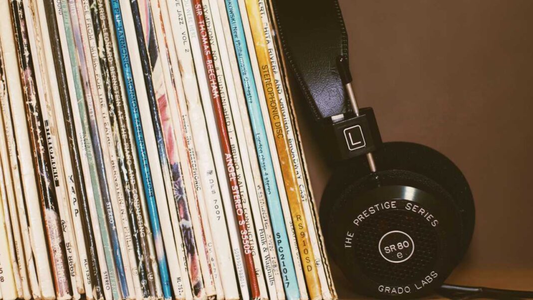Discos de vinilo alineados junto a unos auriculares negros con la inscripción Grado Labs y SR80 e sobre fondo marrón.