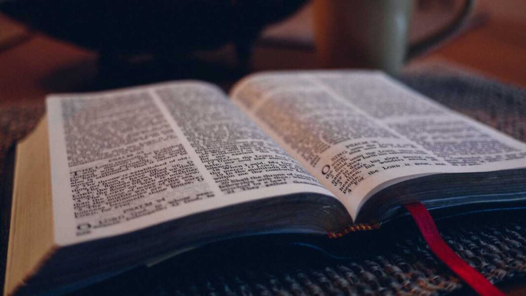 Libro abierto con páginas de texto denso en dos columnas, cinta roja y fondo desenfocado con una taza.