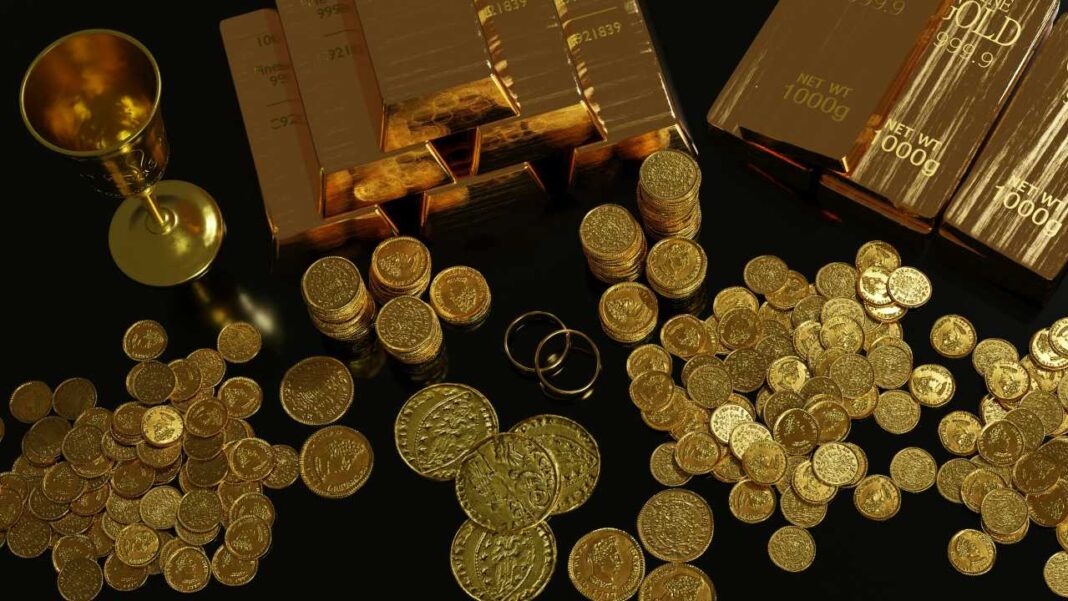 Lingotes de oro apilados junto a muchas monedas doradas, una copa y dos anillos sobre una superficie oscura y reflectante.
