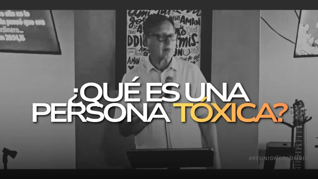 Hombre con gafas habla frente a un micrófono; sobre la imagen aparece el texto ¿Qué es una persona tóxica? y se ven carteles y una guitarra al fondo.